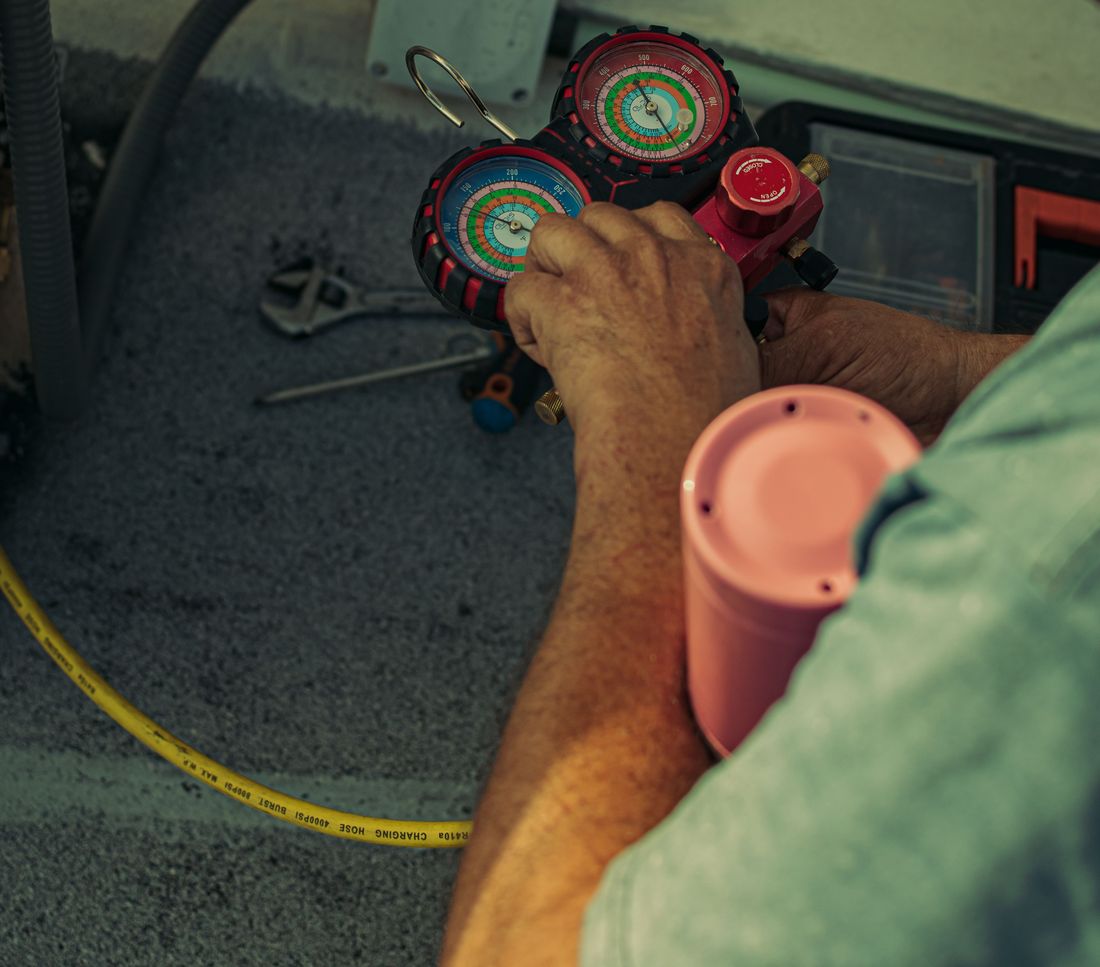 A technician’s hands holding a manifold gauge set connected to an R-410A charging hose